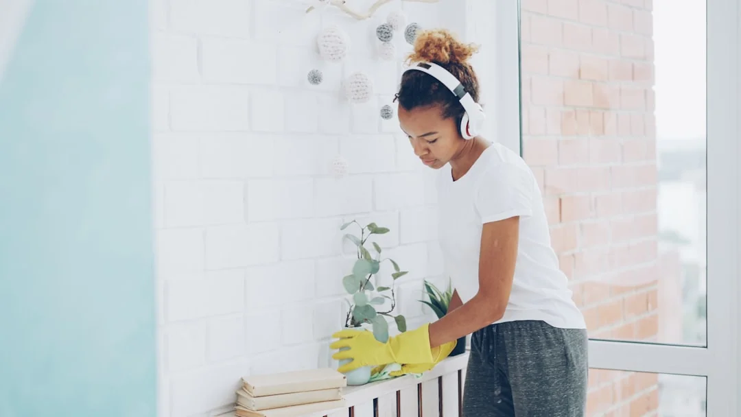 a-woman-in-a-green-shirt-and-black-gloves-vacuuming-a-gray-ottoman-5txz228u4eo